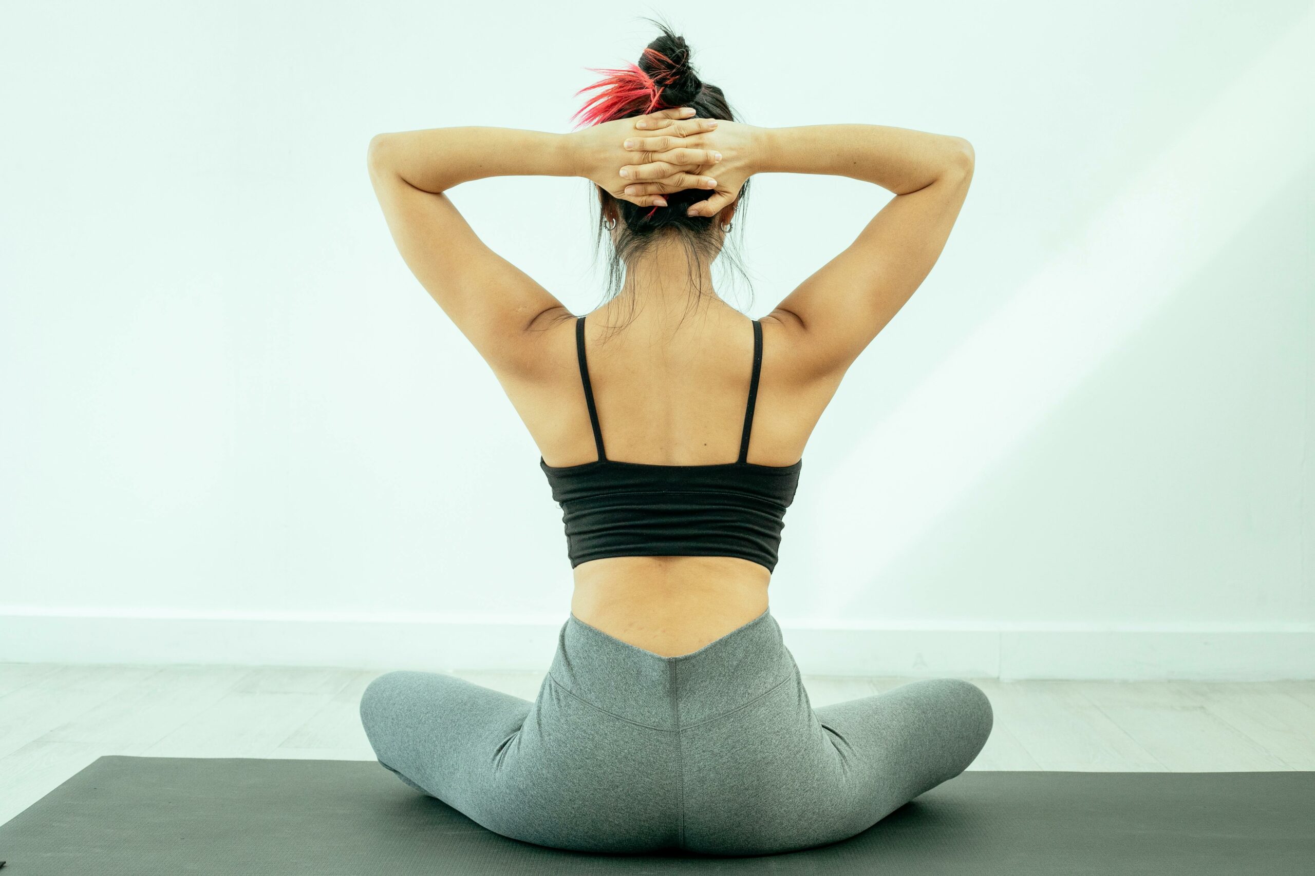 Une femme assise de dos réalisant des étirements du haut du dos.