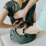 Image d'une femme assise qui montre sa douleur dans le dos, en se faisant manipuler par un ostéopathe.
