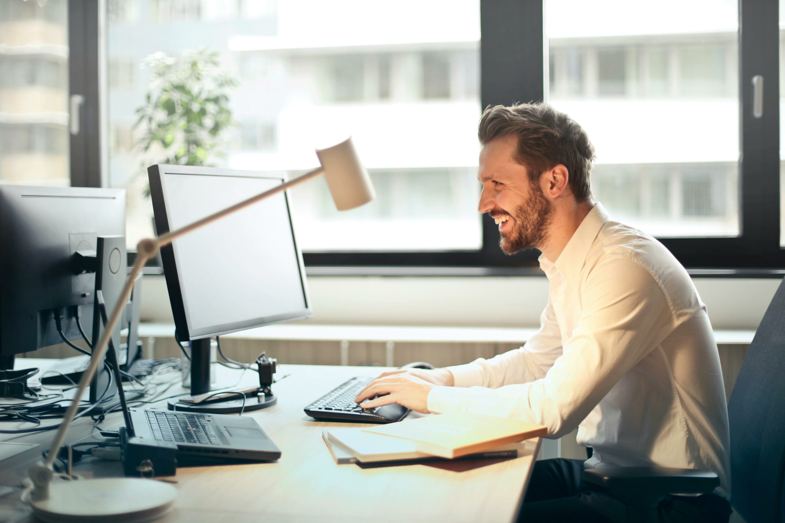 Un homme assis à son bureau face à son ordinateur et souriant.