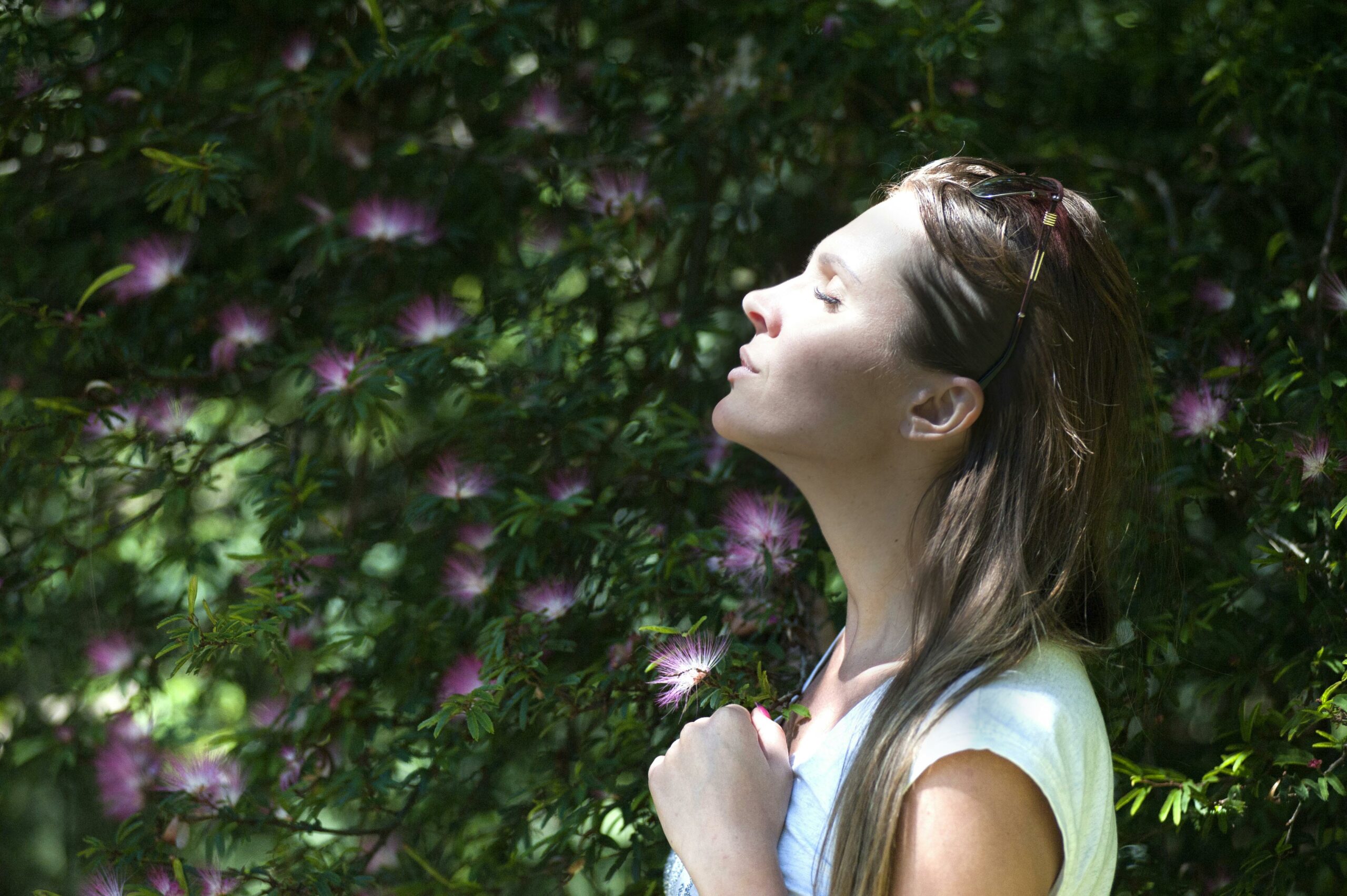 Femme sereine, debout face à la nature, les yeux fermés et un léger sourire, illustrant la détente et l’apaisement apportés par l’ostéopathie dans la gestion du stress.